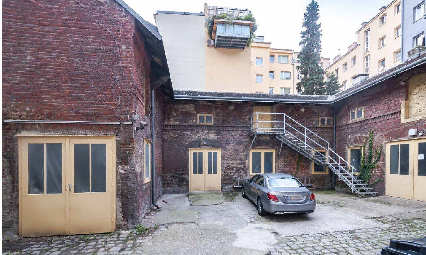 Alter Innenhof mit Backsteingebäuden, einer Außentreppe und parkendem Auto.