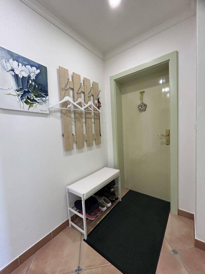 Freundlicher Flur mit Schuhregal, Garderobe und einer hellen Eingangstür.