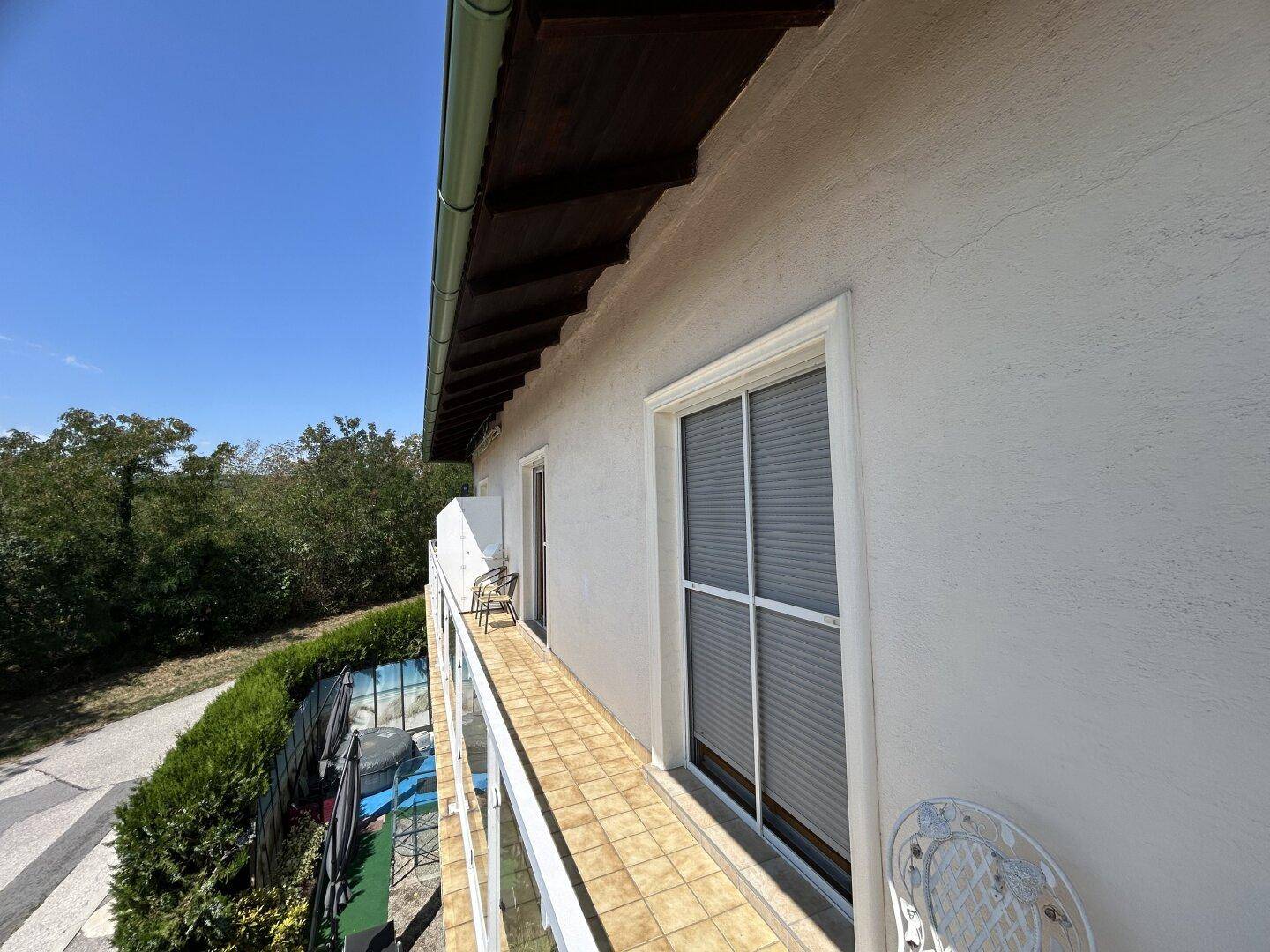 Langer, schmaler Balkon mit Fliesenboden und Blick auf die grüne Umgebung.
