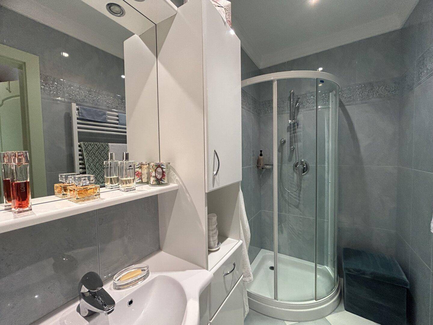Modernes Badezimmer mit Duschkabine, Waschbecken und Spiegelschrank, hell gefliest.