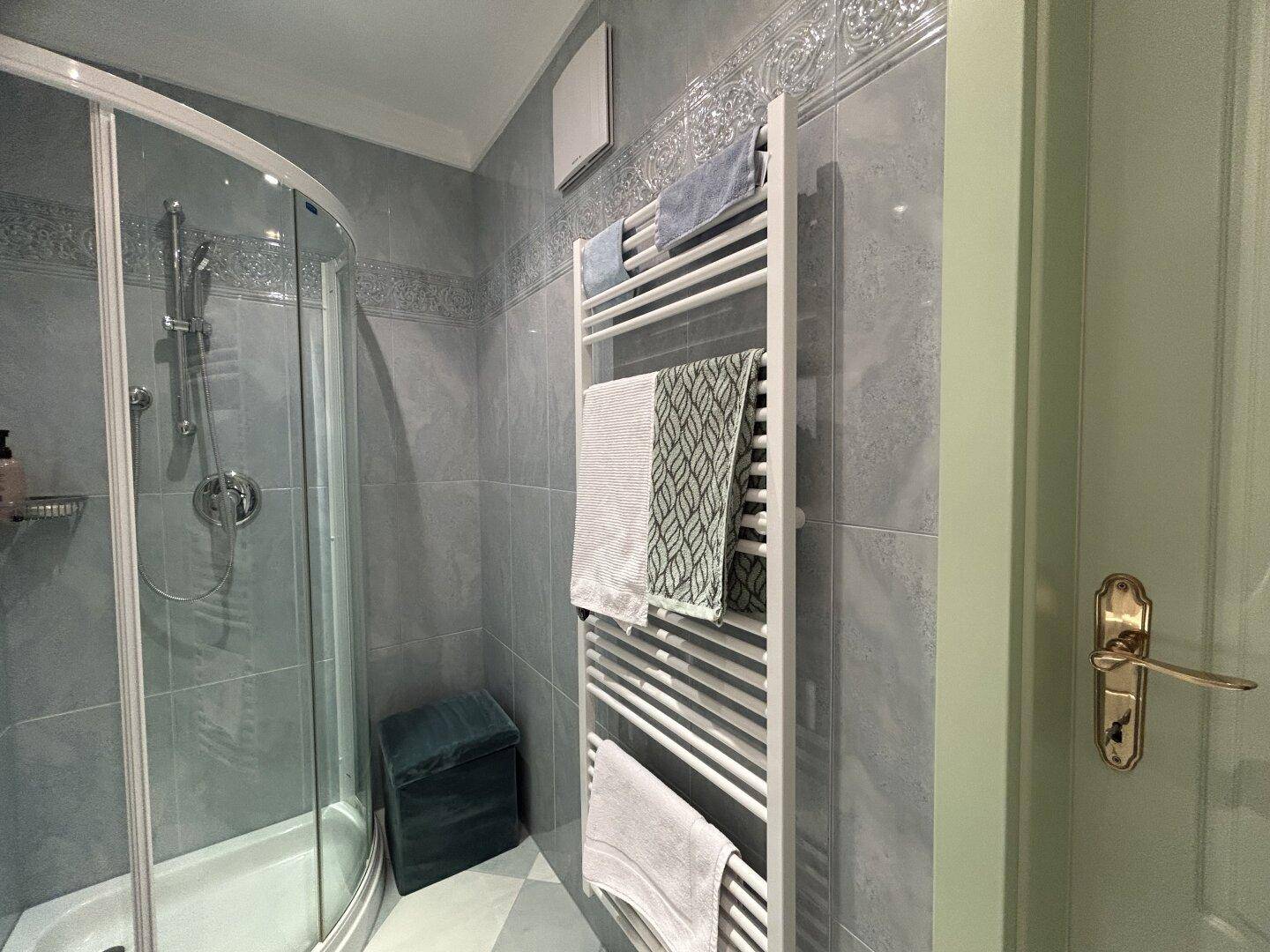 Modernes Badezimmer mit Duschkabine, grauen Fliesen und beheiztem Handtuchhalter.