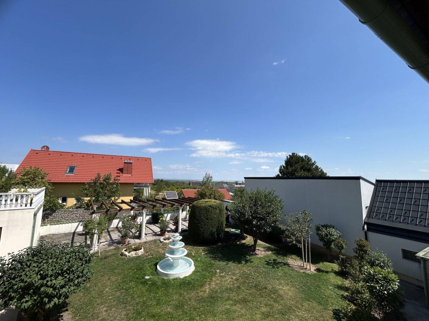 Gepflegter Garten mit Rasenfläche, Bäumen und einem dekorativen mehrstufigen Brunnen.