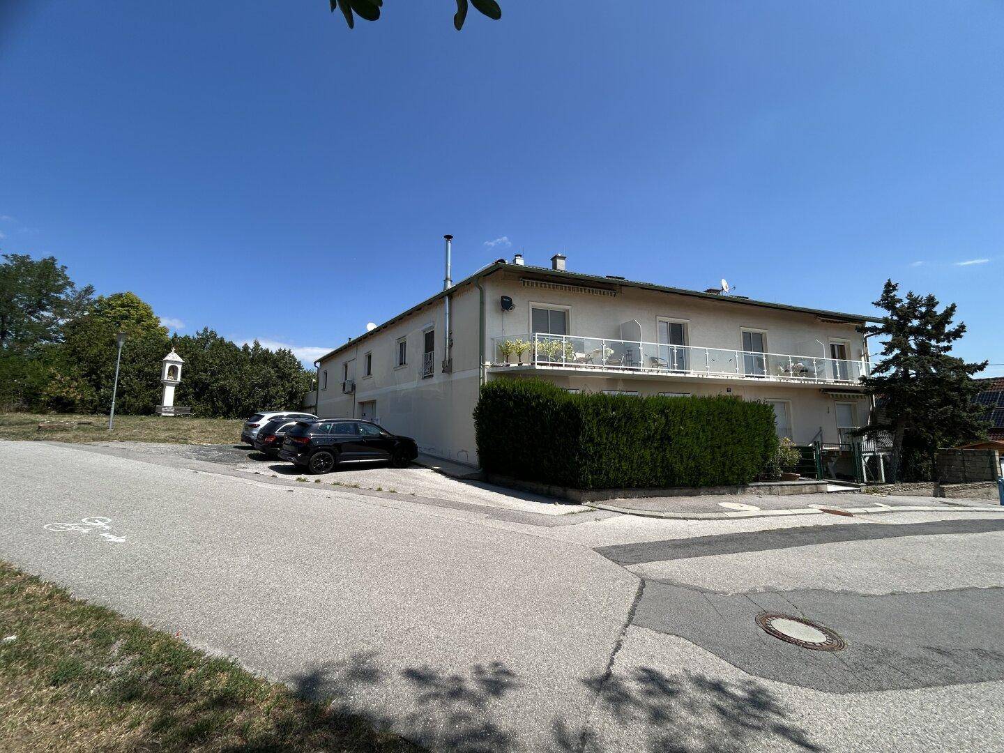 Seitenansicht des Hauses mit Parkplätzen und einem kleinen Denkmal in der Ferne.