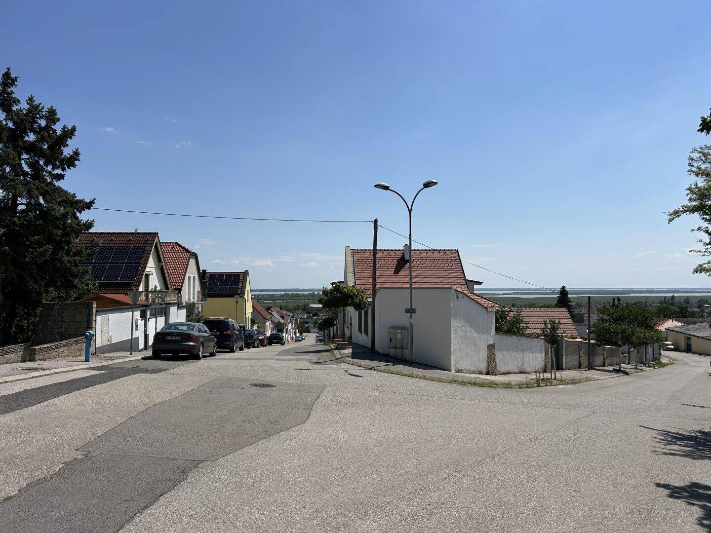 Straßenansicht einer Wohngegend mit Häusern und einem weiten Blick auf ein Gewässer in der Ferne.