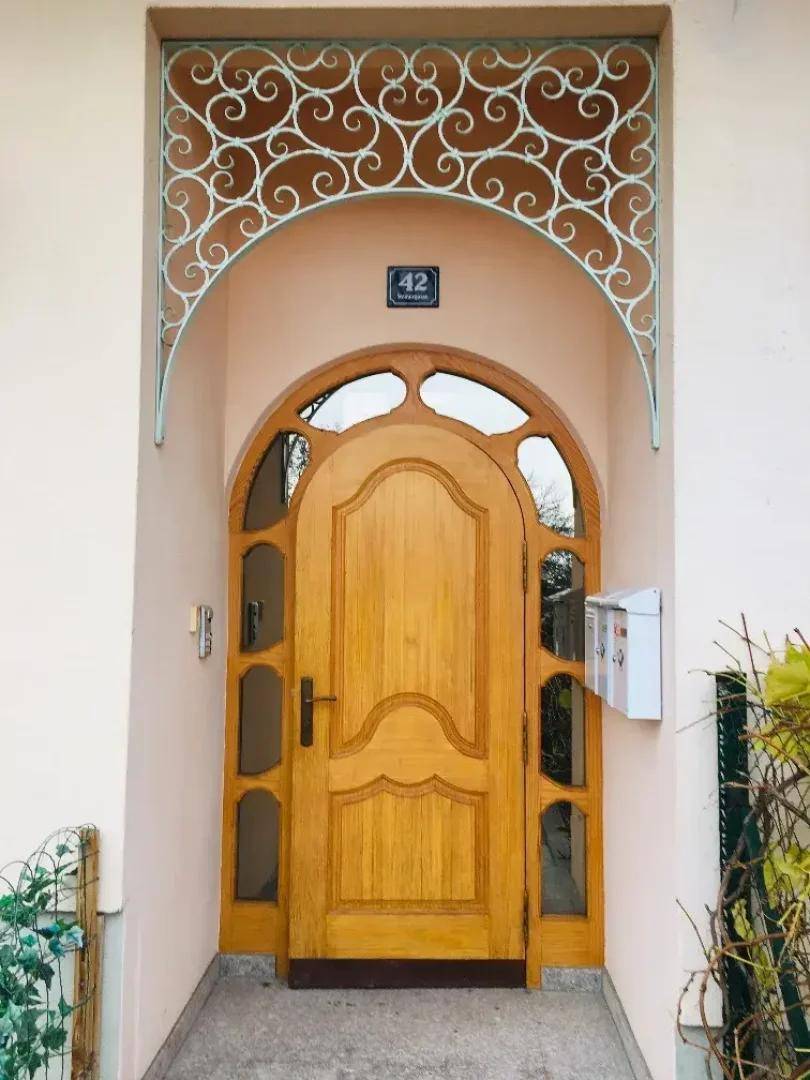 Traditioneller Hauseingang mit Holztür, Bogen und dekorativem Metallgitter über dem Eingang.