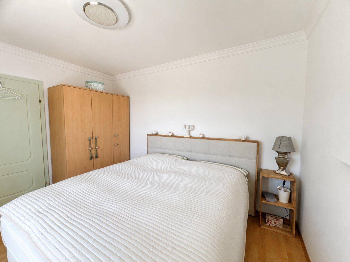 Schlafzimmer mit Doppelbett, Holzschrank und hellem Holzboden, freundlich und funktional.