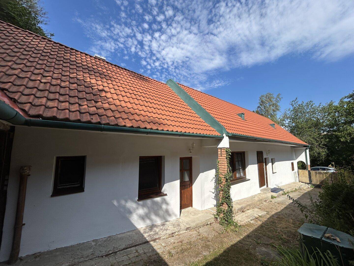 Seitenansicht des Hauses mit rotem Ziegeldach und einem gepflasterten Weg unter blauem Himmel.