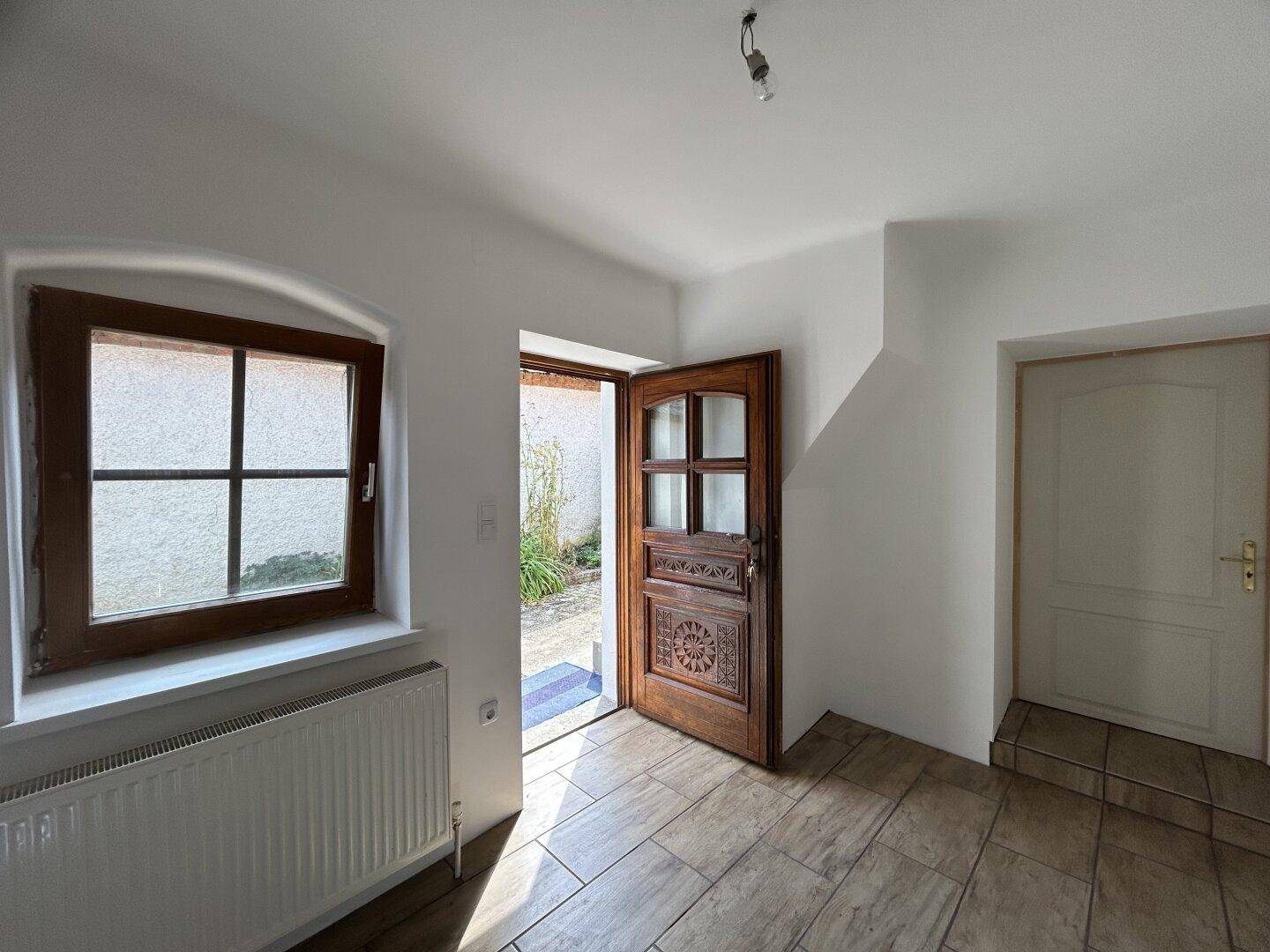 Heller Eingangsbereich mit gefliestem Boden, Holztür und Fenster mit Heizkörper.