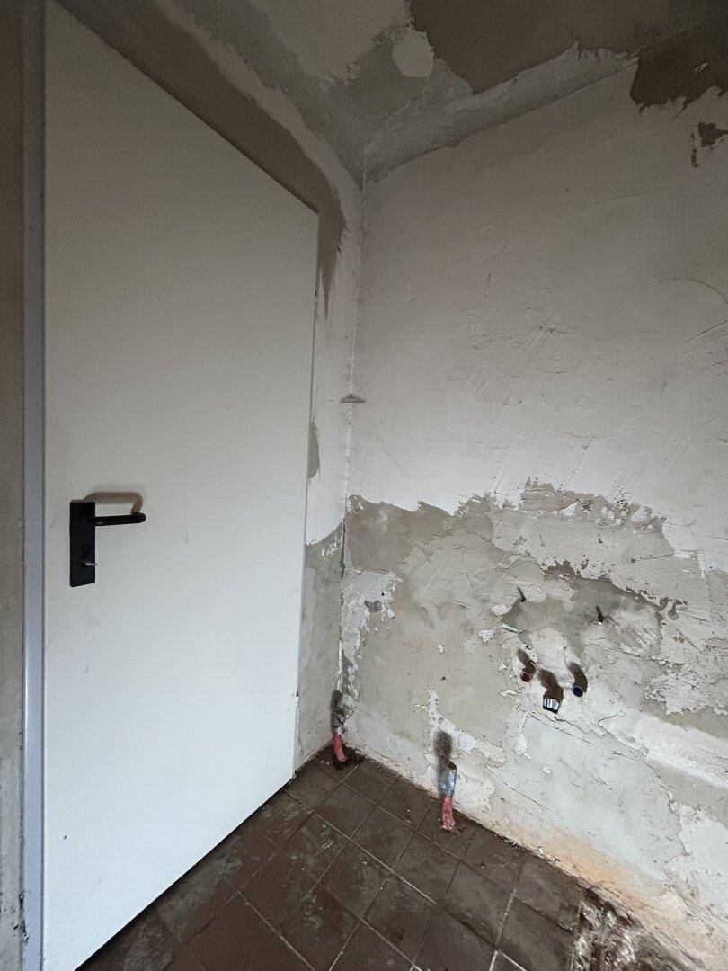 Unfertiger Raum mit Rohleitungen und unebenen Wänden, bereit für den Ausbau.
