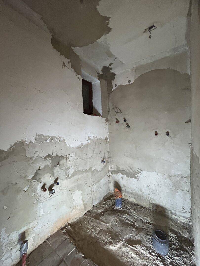Rohbau-Raum mit sichtbaren Installationen und unfertigen Wänden, wartet auf Fertigstellung.