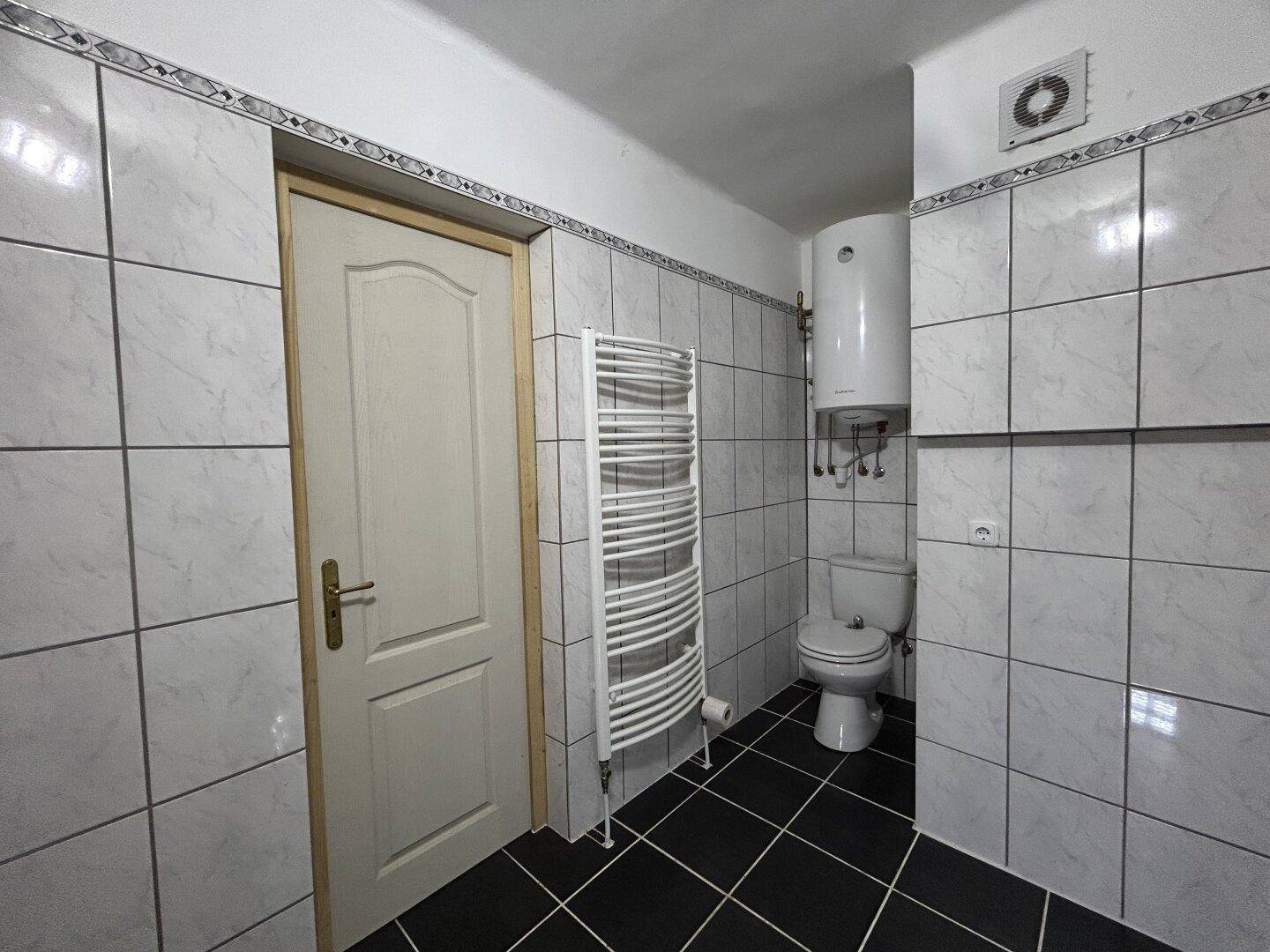 Badezimmer mit Toilette, Warmwasserboiler und beheiztem Handtuchhalter in gefliestem Raum.