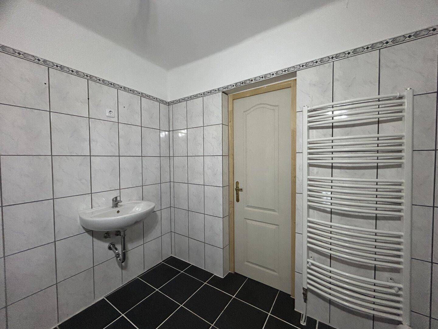 Badezimmer mit Waschbecken, beheiztem Handtuchhalter und weiß-schwarzen Fliesen.