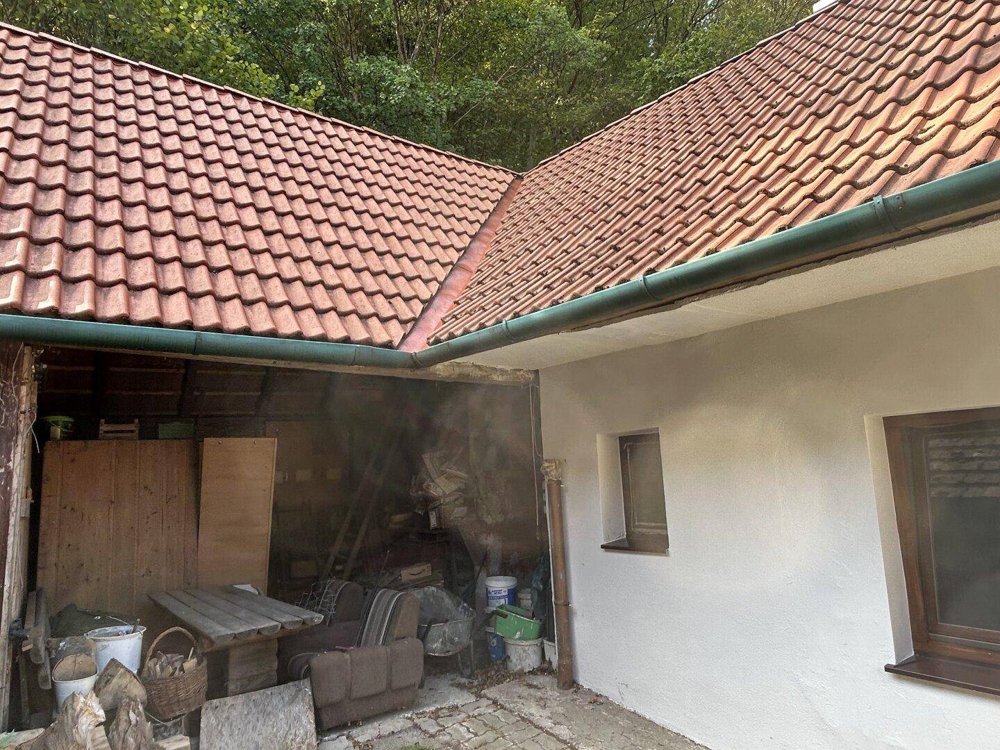 Offener Lagerbereich neben dem Haus mit Holzverkleidung und verschiedenen Gegenständen.
