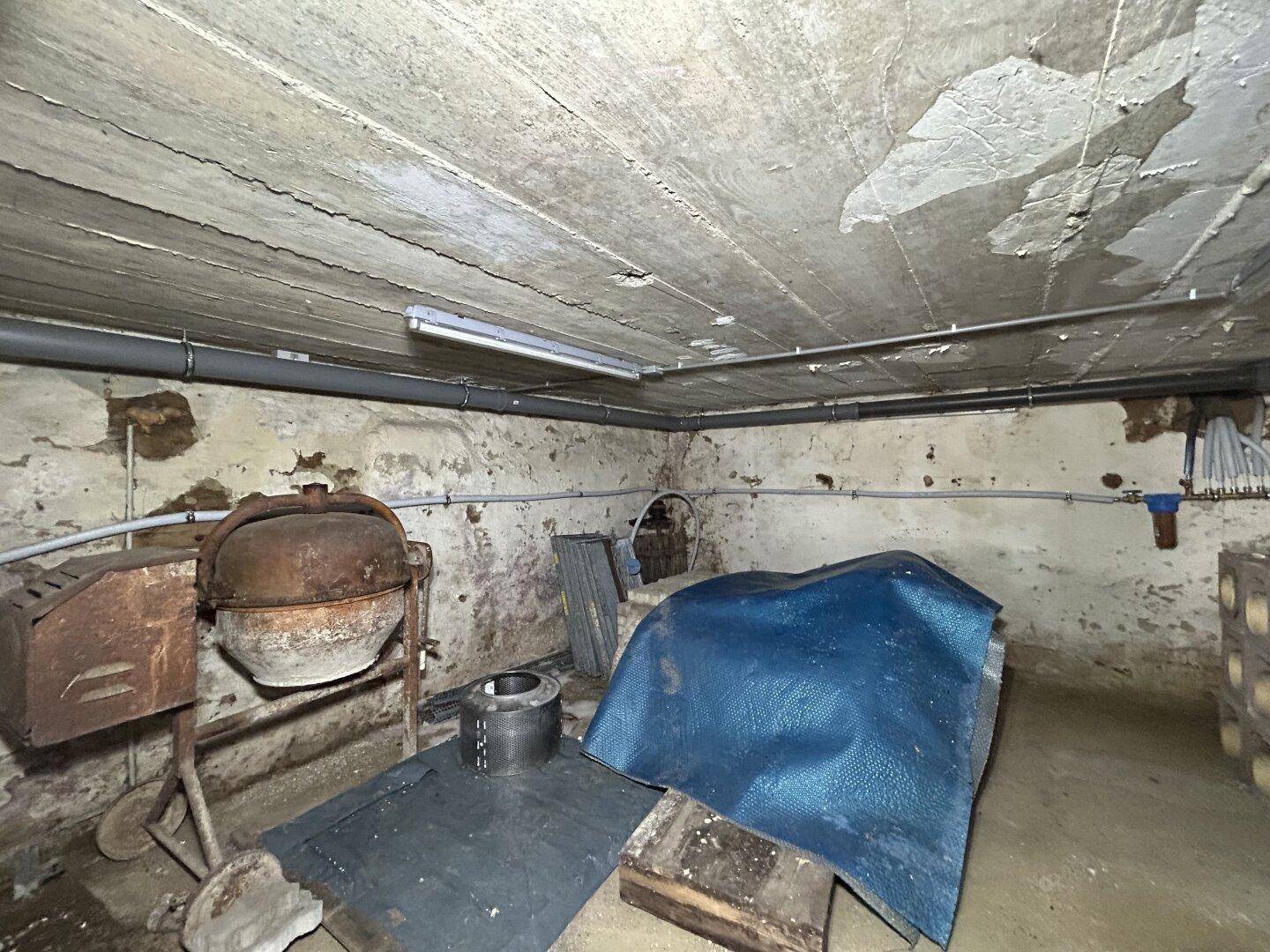 Unfertiger Kellerraum mit Betonboden und -decke, Zementmischer und Lagergegenständen.