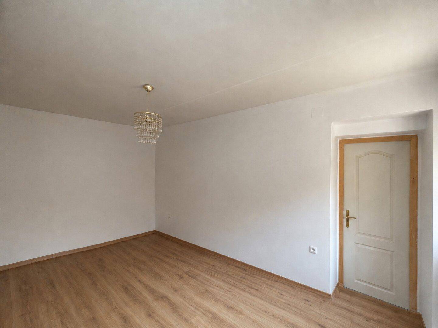 Leerer Raum mit Laminatboden und weiß gestrichenen Wänden, bereit zur individuellen Gestaltung.