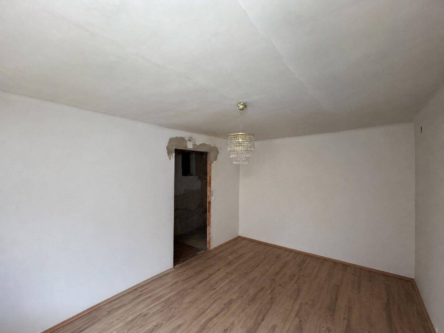 Raum mit Laminatboden und offenem Durchgang zu einem weiteren Bereich, ideal für Renovierungsprojekte.