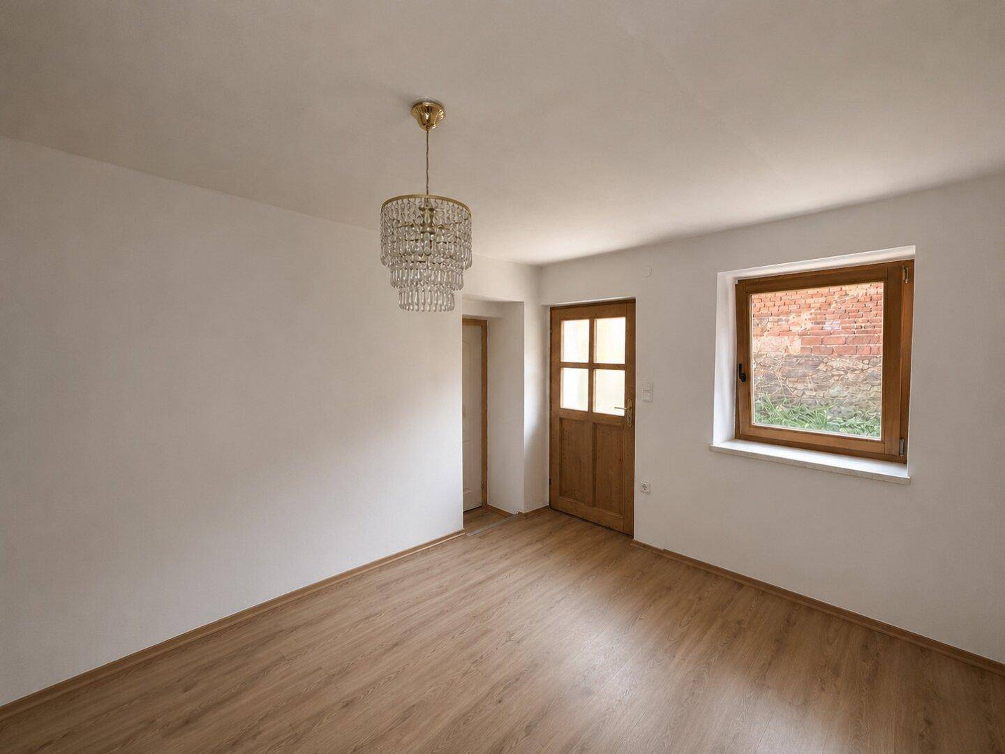 Heller Raum mit Laminatboden, Fenster, Holztür und einem eleganten Kronleuchter.
