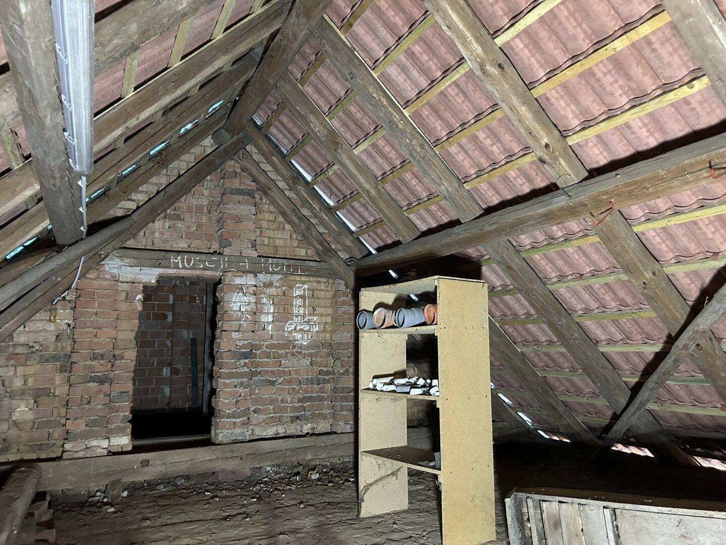 Rustikaler Dachboden mit freiliegenden Holzbalken und unverputzten Ziegelwänden, ideal als Lagerraum.