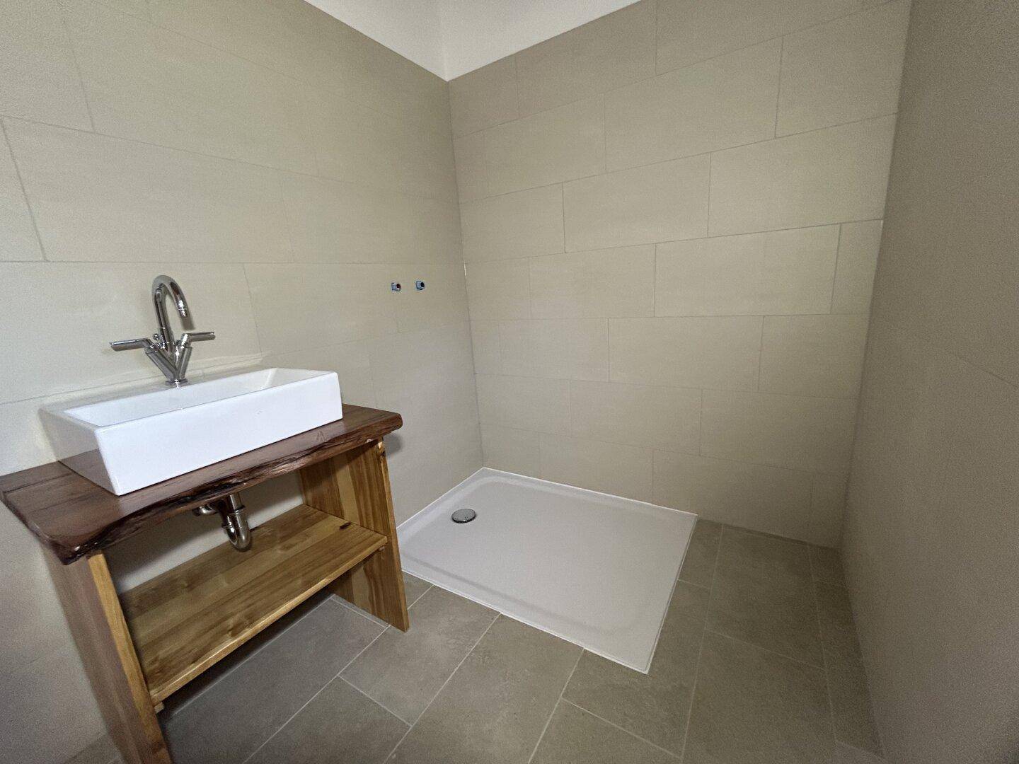 Modernes Badezimmer mit Aufsatzwaschbecken, Holztisch und ebenerdiger Dusche.