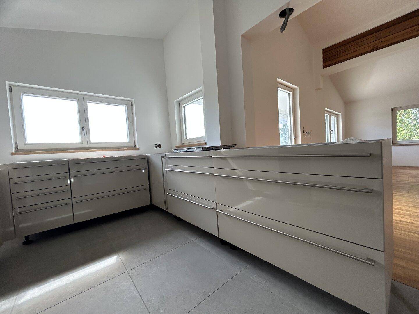 Moderne Küche mit hellen Schränken, Fliesenboden und viel Tageslicht.