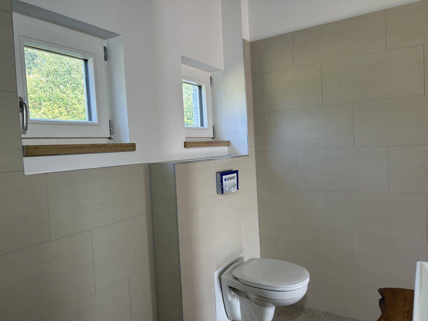 Helles WC mit Wandtoilette, kleinem Fenster und modernen Fliesen.