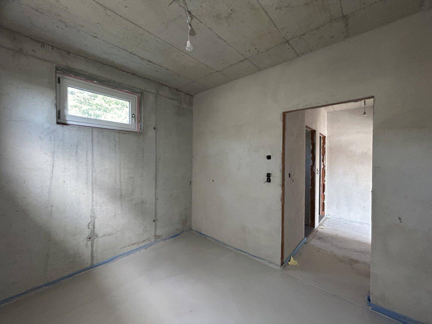 Rohbau eines Raumes mit Betonwänden, kleinem Fenster und Türöffnung.