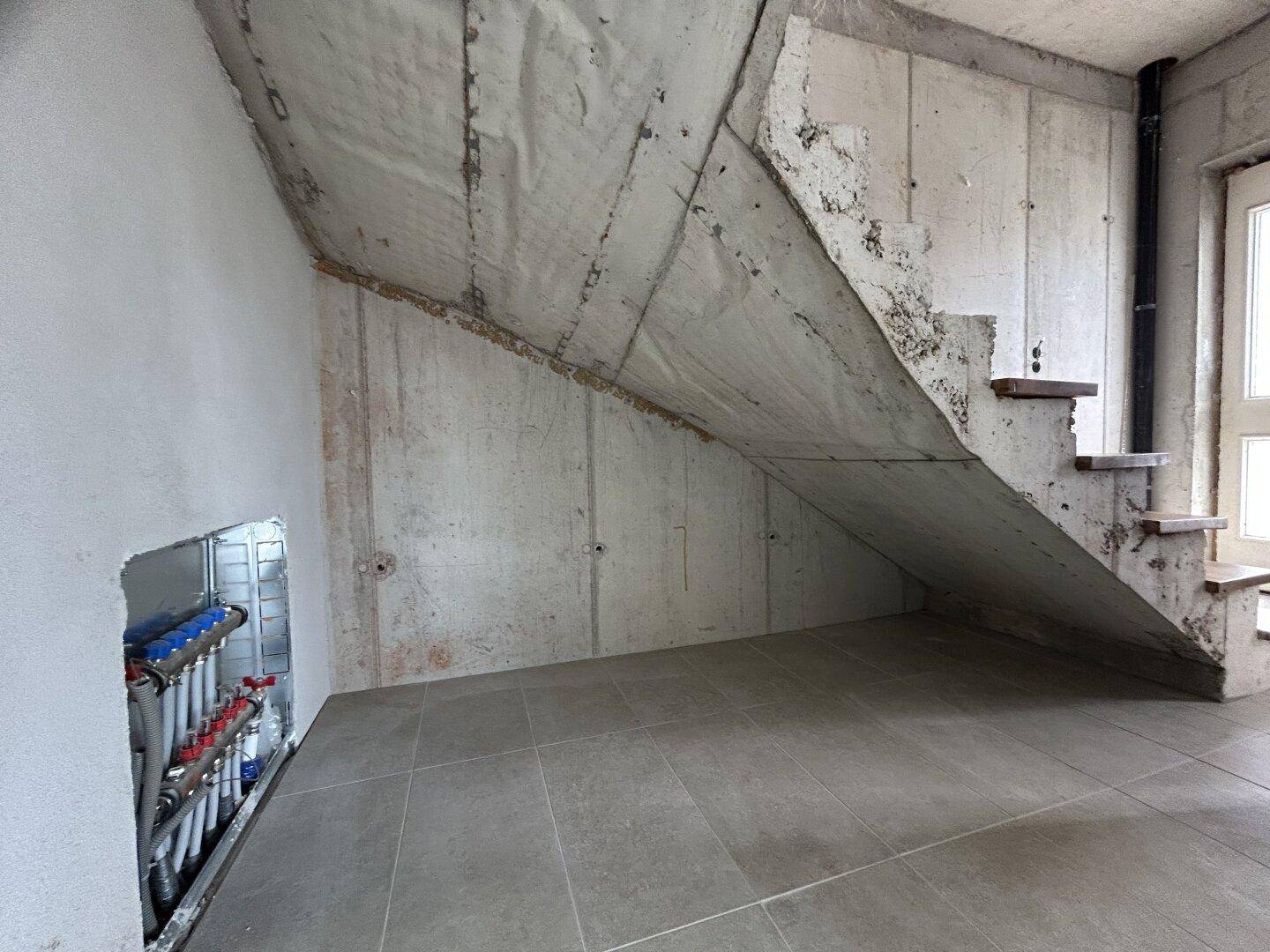 Treppenbereich im Rohbau mit Betonstufen und sichtbaren Heizungsverteilern.