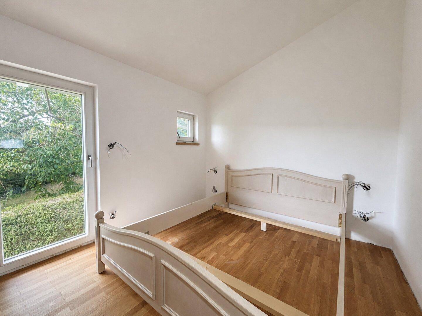 Schlafzimmer mit Parkettboden und Zugang zu einem französischen Balkon mit Gartenblick.