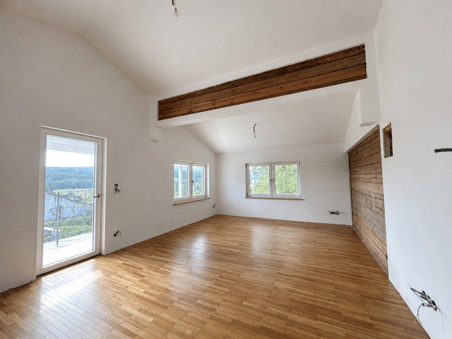 Heller Wohnbereich mit Holzbalken, Parkettboden und Zugang zu einem französischen Balkon.