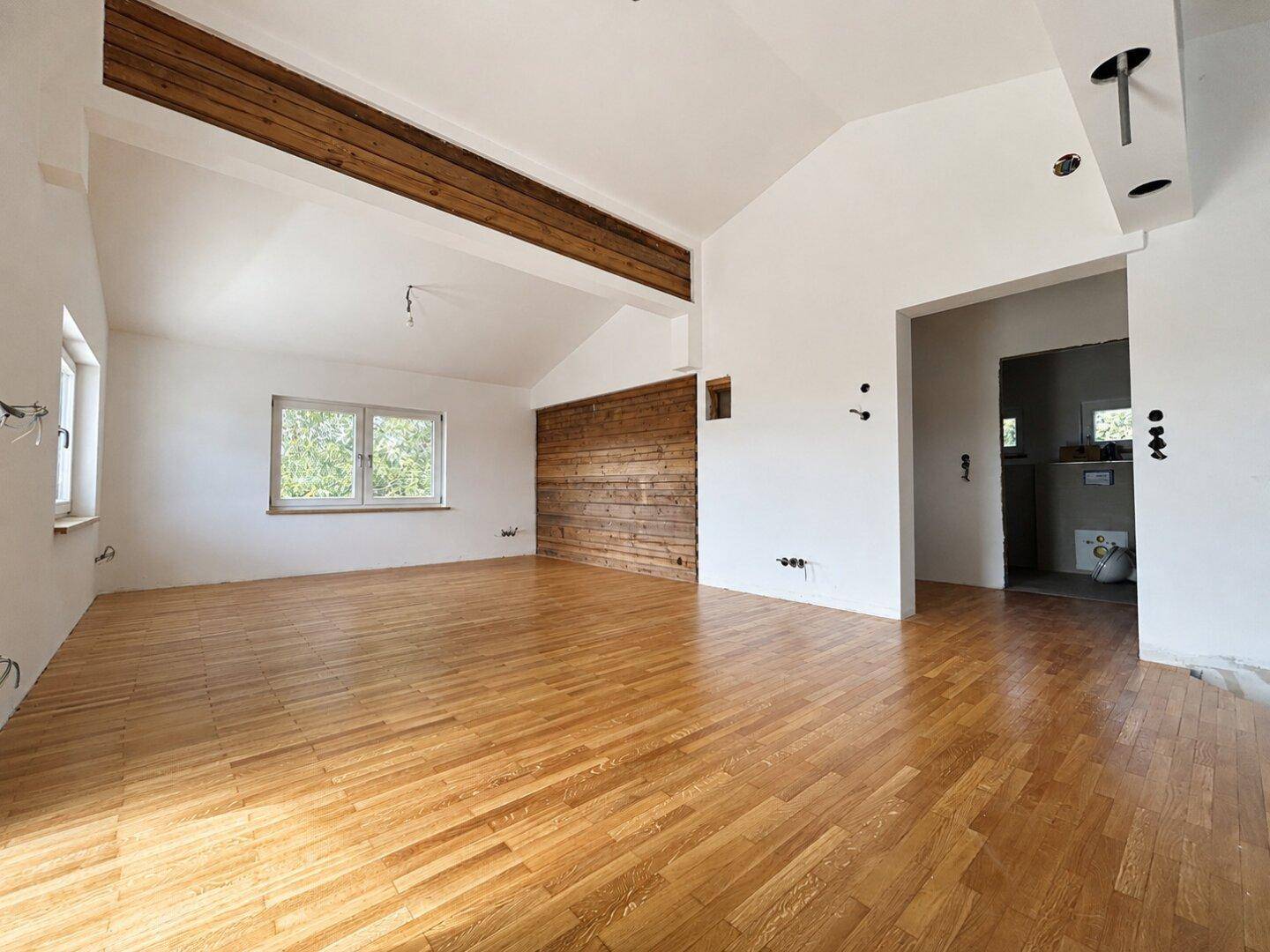 Geräumiger Wohnbereich mit Holzbalken, Parkettboden und einer Holzwand.