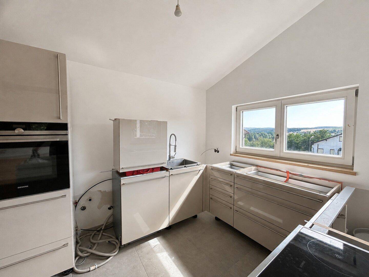 Küche in heller Farbe mit Einbaugeräten und Fenster mit weitem Ausblick.