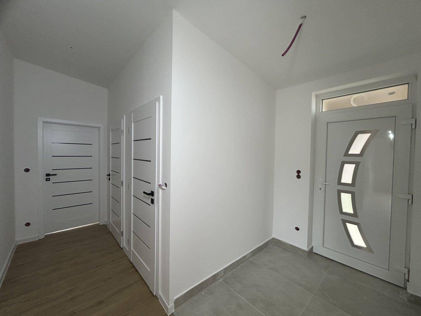 Heller Eingangsbereich mit moderner Haustür und mehreren Innentüren, ausgestattet mit Fliesen- und Laminatboden.