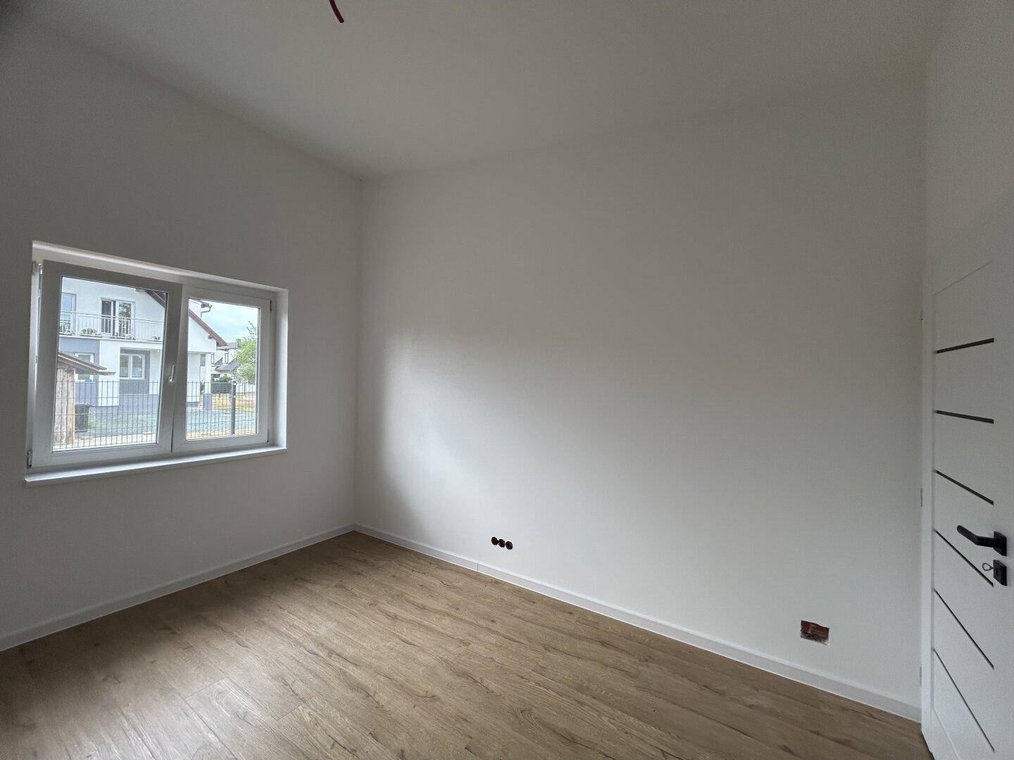 Leeres Schlafzimmer mit hellem Laminatboden und einem Fenster, das Tageslicht hereinlässt.