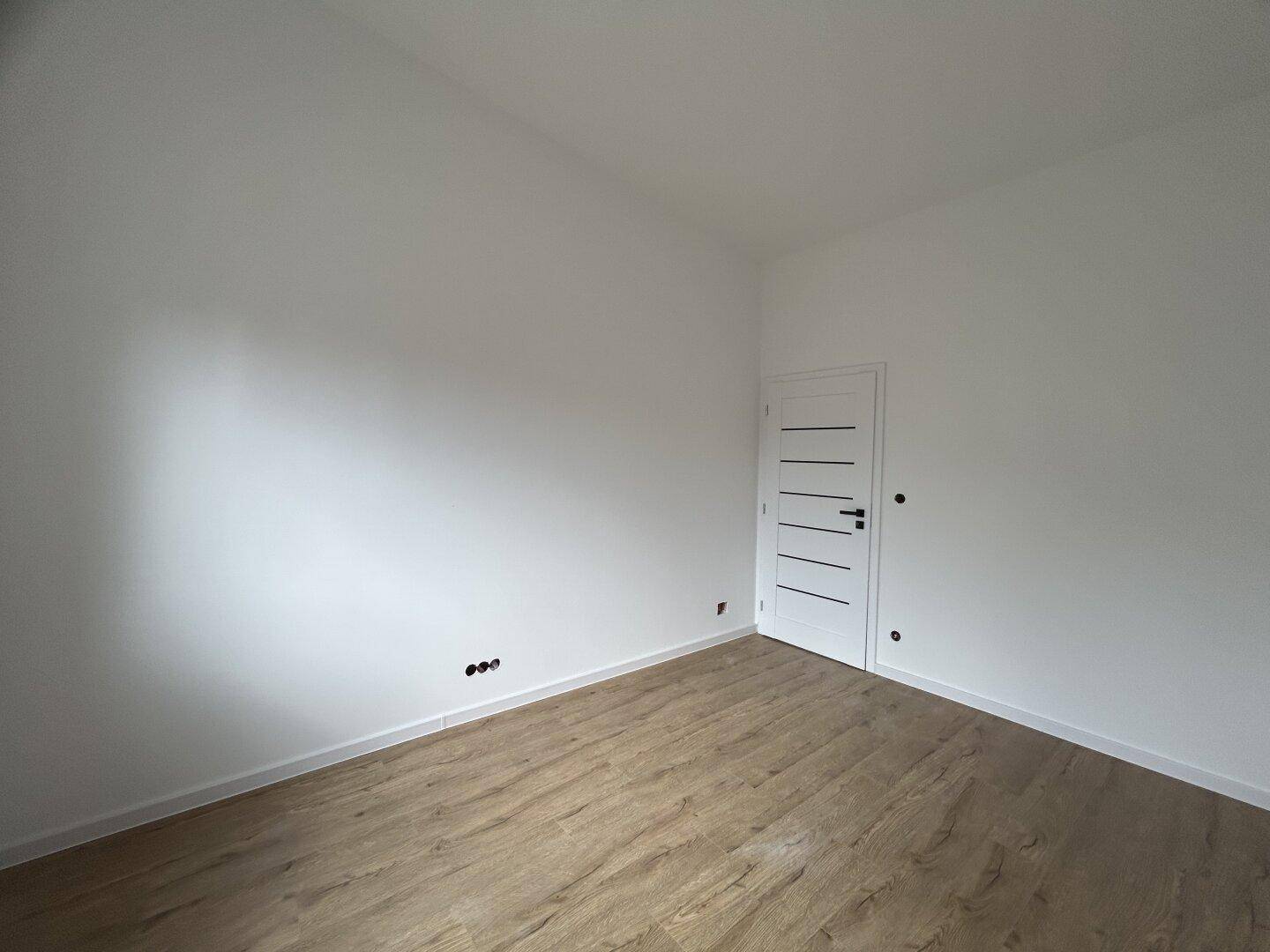 Unmöbliertes Zimmer mit neuem Laminatboden und einer modernen weißen Tür, bereit zum Einzug.