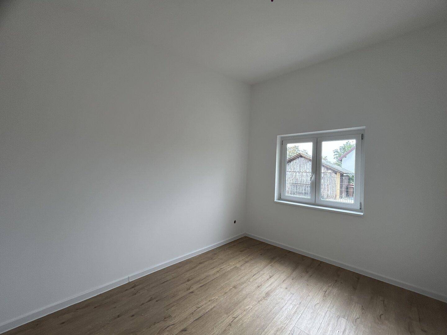Helles Zimmer mit Laminatboden und einem Fenster, das einen Blick auf die Umgebung bietet.