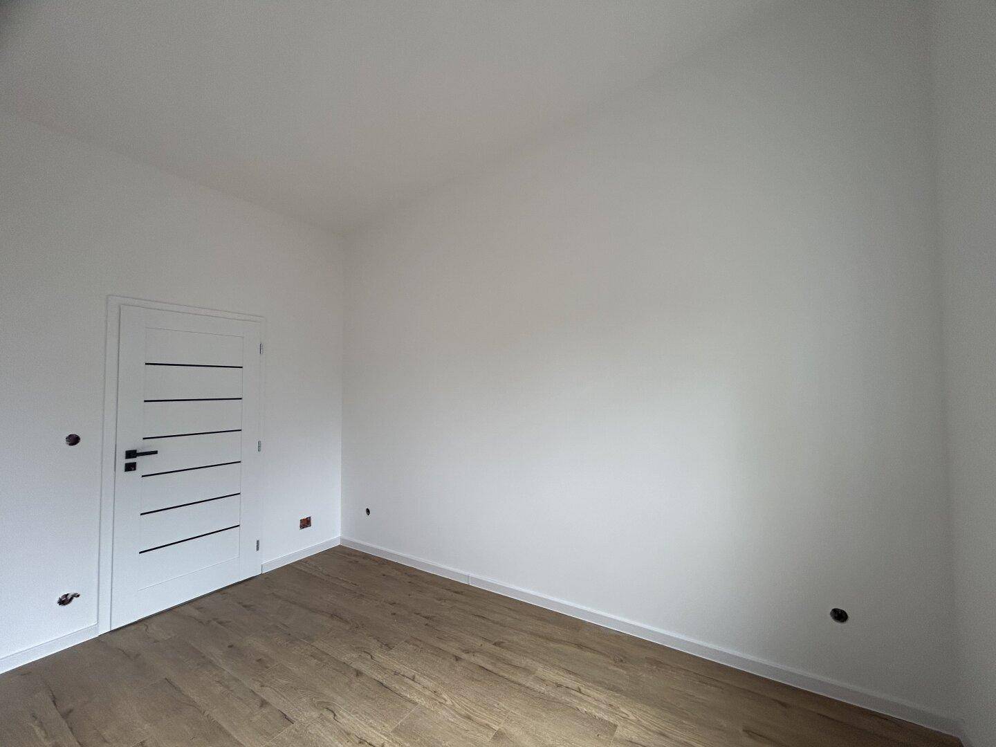 Leeres Zimmer mit sauberem Laminatboden und einer modernen Innentür, ideal für individuelle Gestaltung.