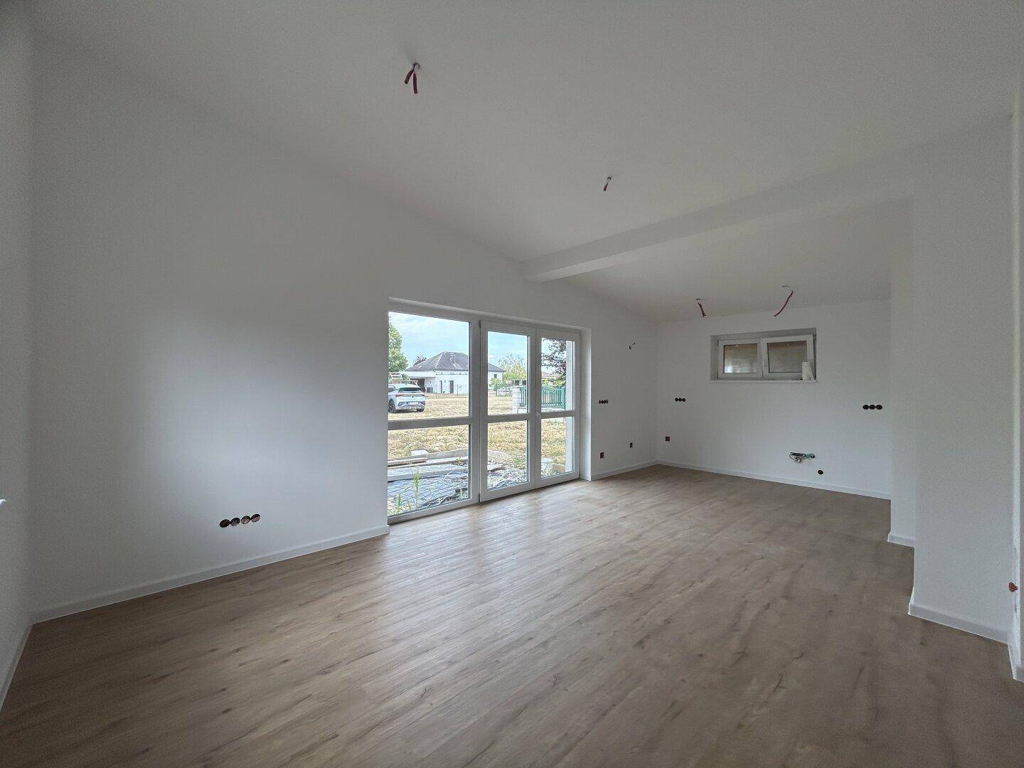 Geräumiges Wohnzimmer mit großen Fenstern und Zugang zum Außenbereich, ausgestattet mit Laminatboden.