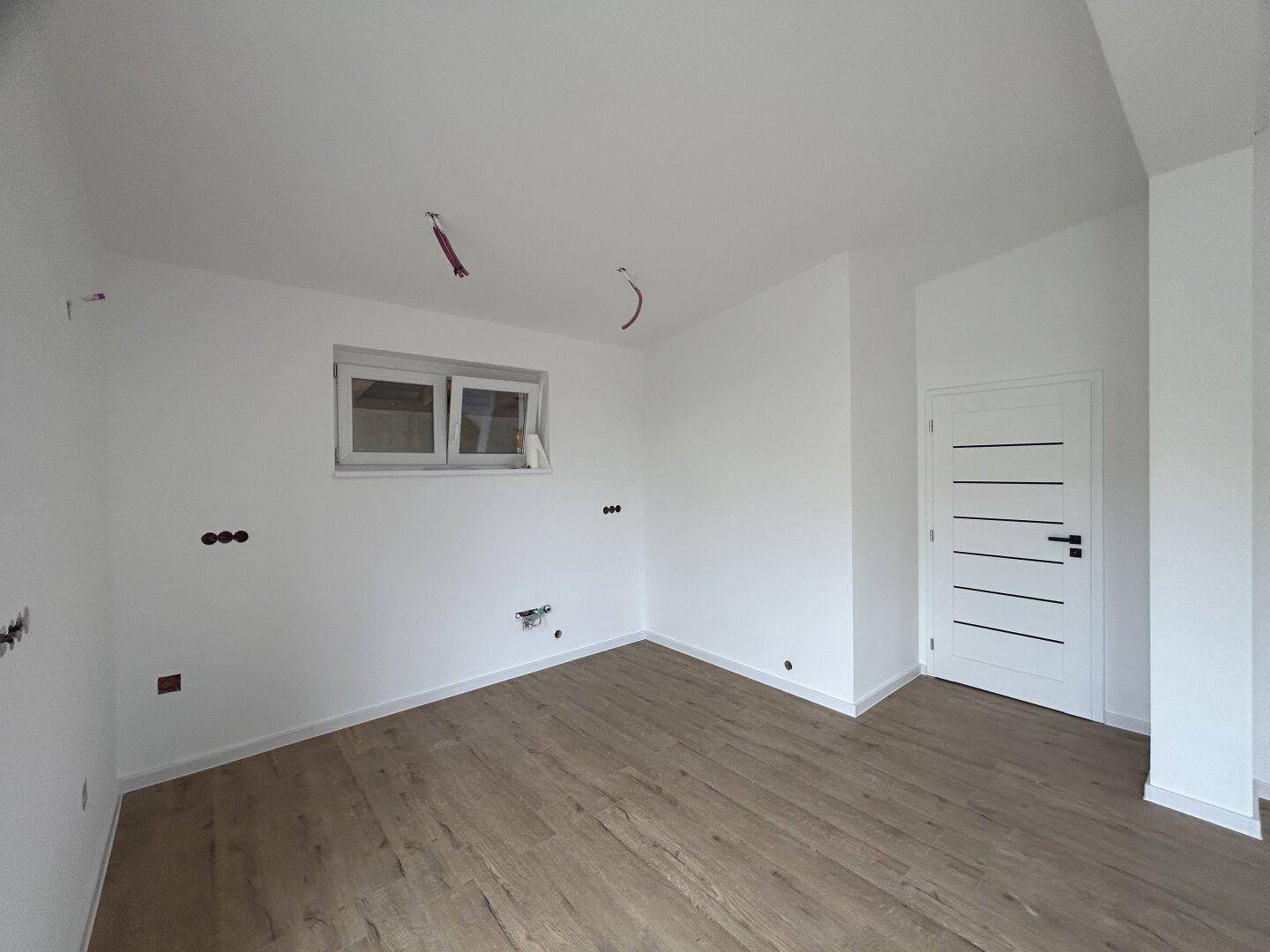 Unmöbliertes Zimmer mit Laminatboden und einem Fenster, das für ausreichend Helligkeit sorgt.