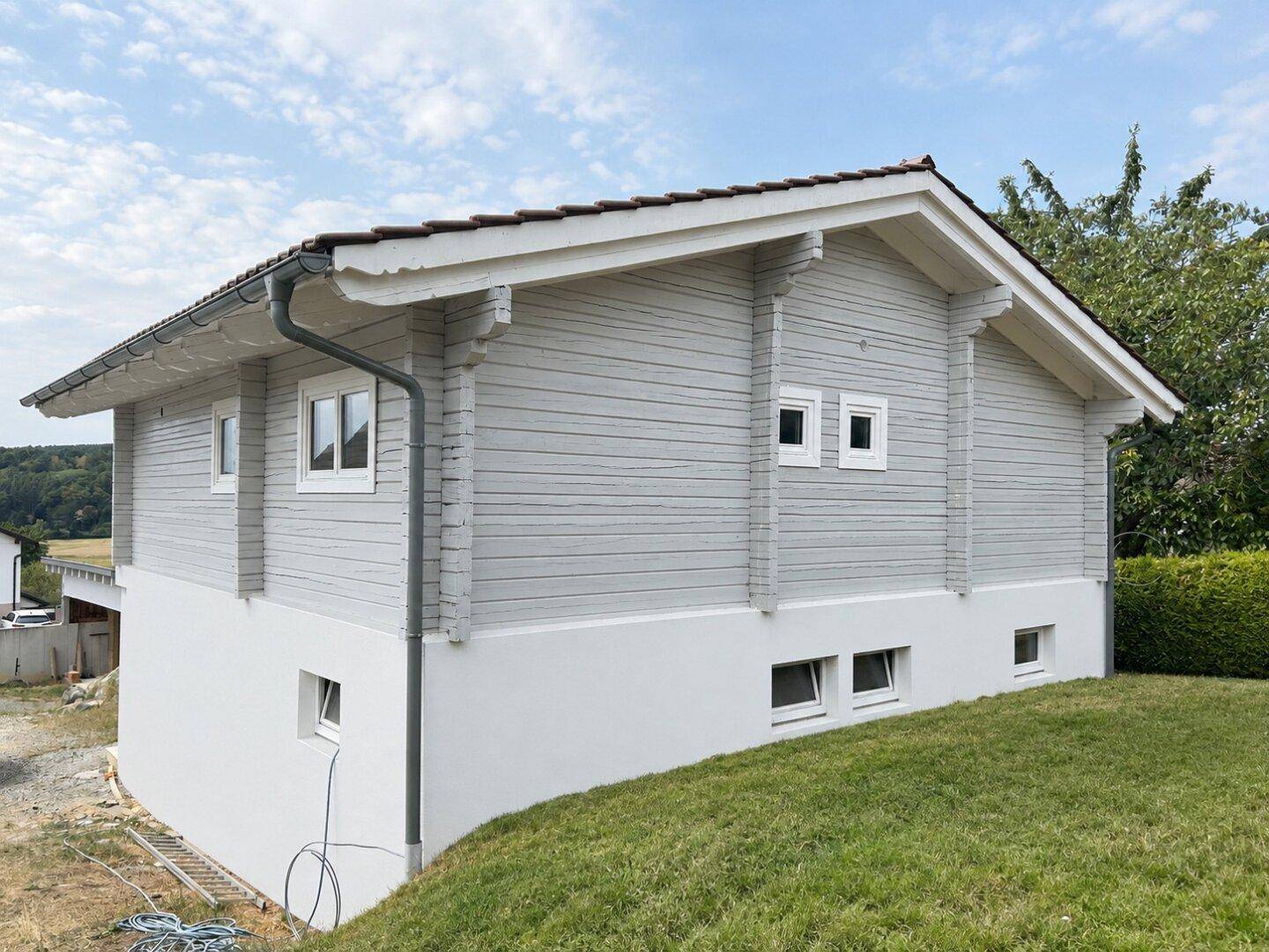 Schräge Seitenansicht des modernen Holzhauses mit weißem Sockel und Dachrinne.