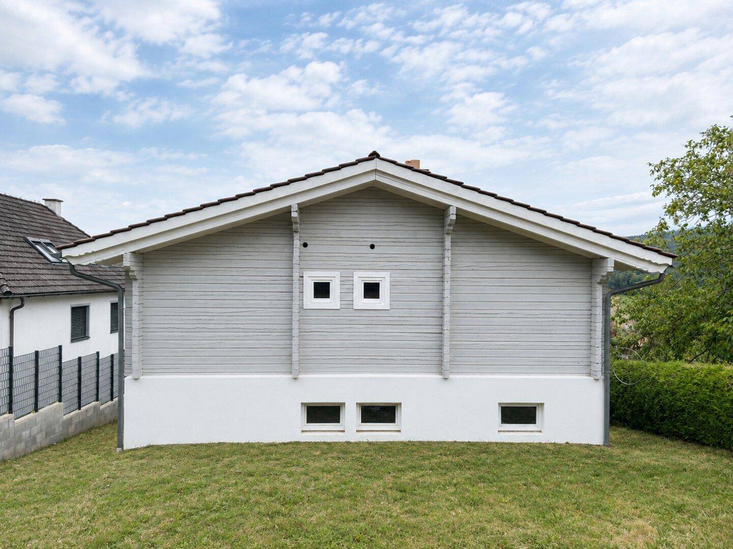 Seitenansicht des Hauses mit Holzfassade und kleinen Fenstern im Untergeschoss.