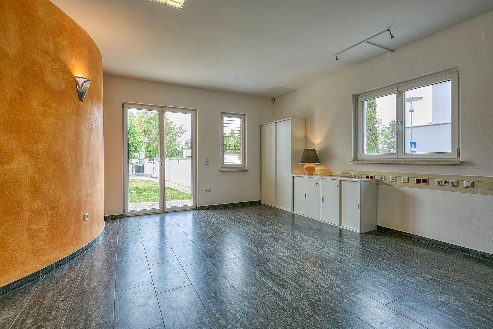 Leerer Raum mit einer orangefarbenen Akzentwand, dunklem Fliesenboden und Zugang zum Garten.