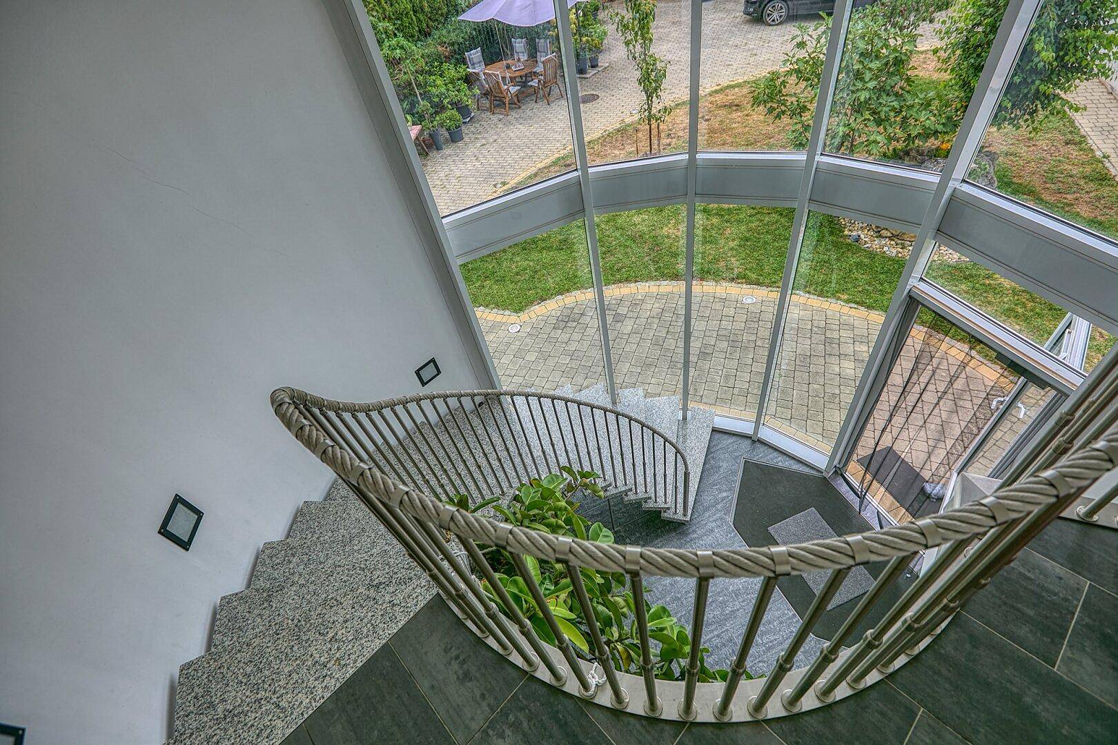Panoramablick vom Treppenhaus auf den Außenbereich mit Rasenfläche und Sitzgelegenheiten.