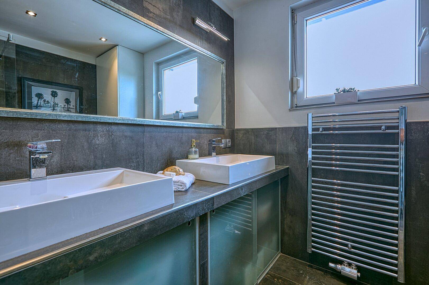 Modernes Badezimmer mit Doppelwaschbecken, großem Spiegel und beheiztem Handtuchhalter.