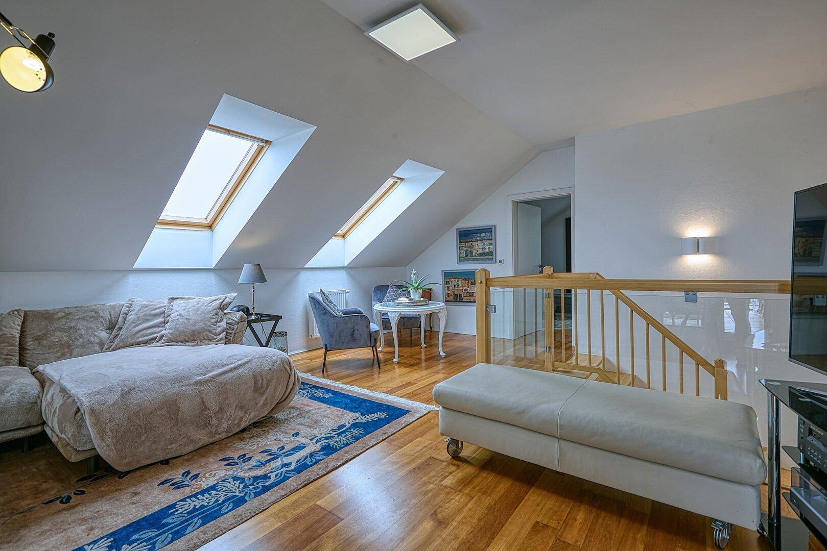 Helles Dachgeschoss-Wohnzimmer mit Holzboden, Dachfenstern und gemütlicher Sitzecke.
