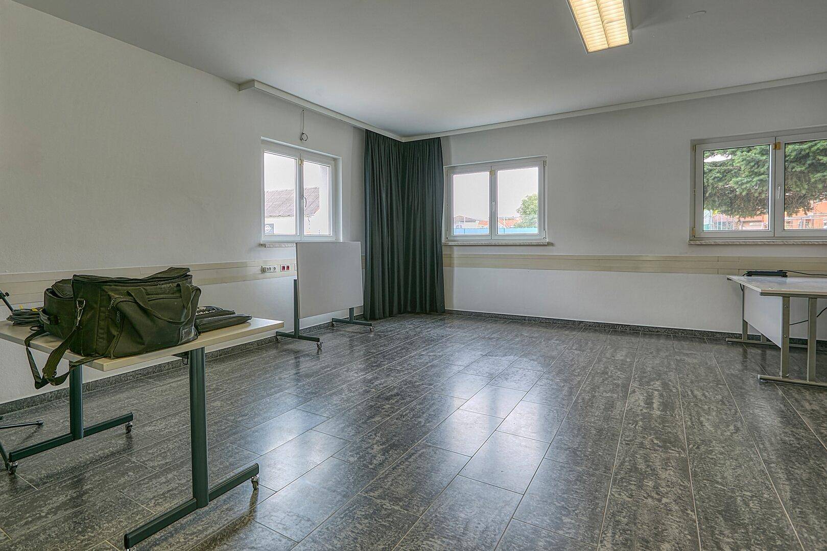 Geräumiger, heller Raum mit großen Fenstern und grauem Fliesenboden, ideal als Büro oder Mehrzweckraum.
