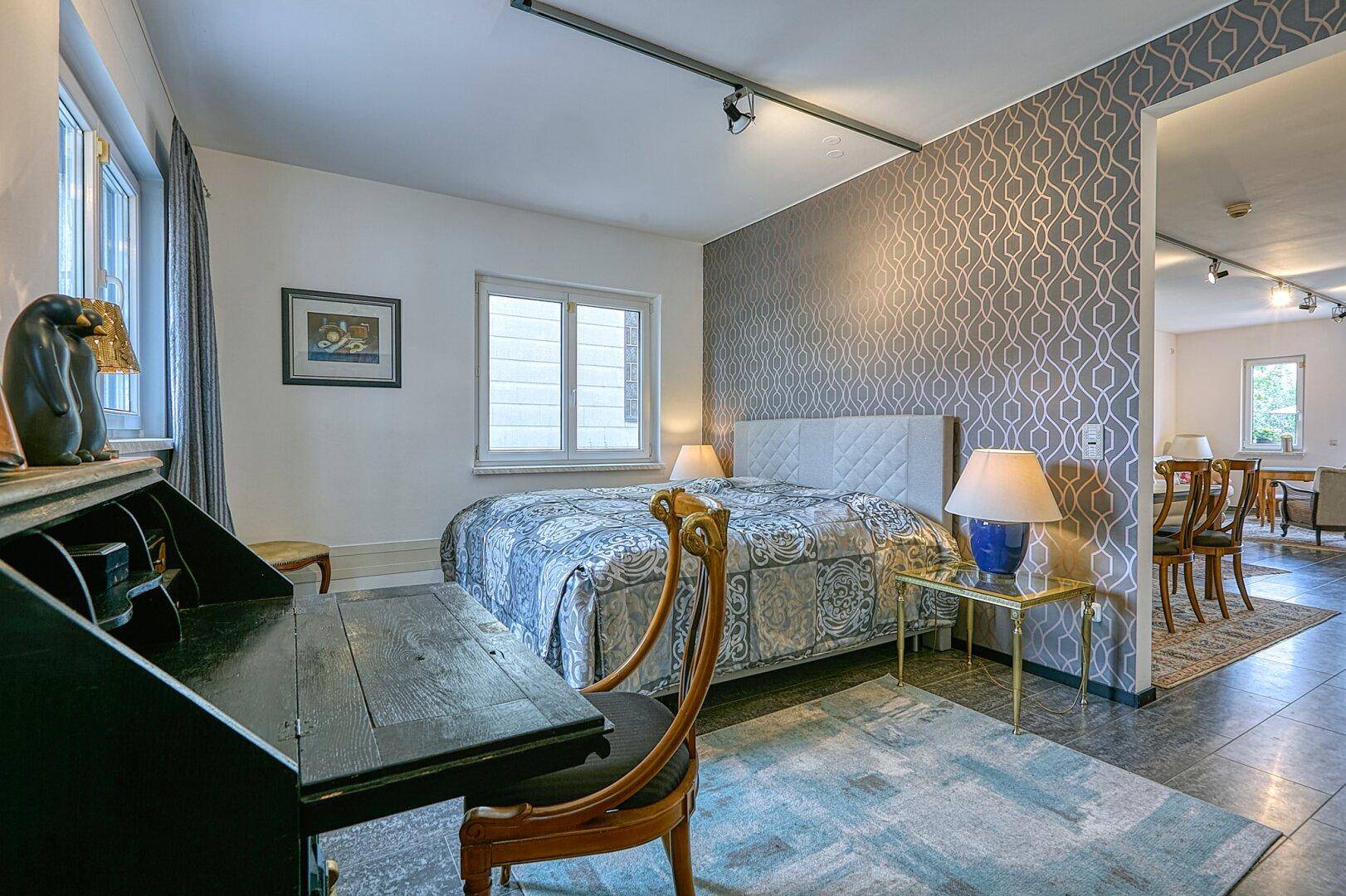 Geräumiges Schlafzimmer mit Doppelbett, Schreibtisch und gemusterter Tapete.