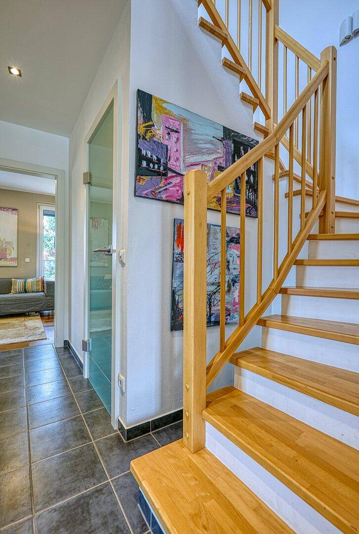 Helle Holztreppe führt in die oberen Stockwerke, mit modernen Kunstwerken an der Wand.
