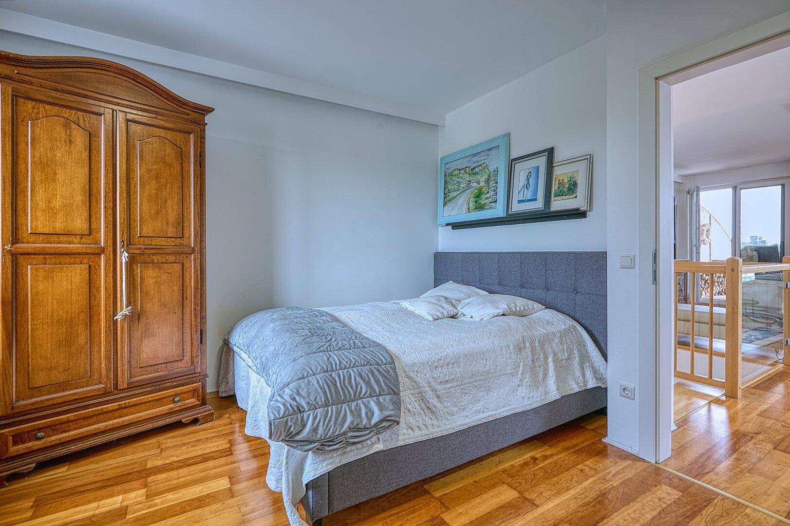 Helles Schlafzimmer mit Holzboden und traditionellem Holzschrank, angrenzend an einen Flur.