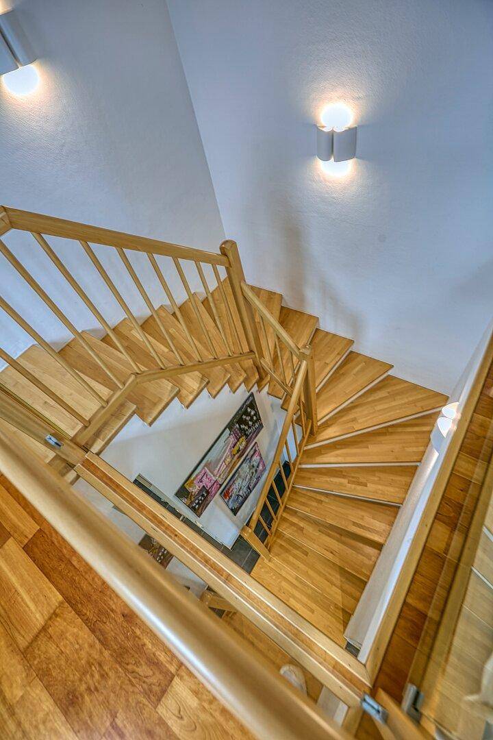 Helle Holztreppe verbindet die Stockwerke, mit modernen Kunstwerken an der Wand.
