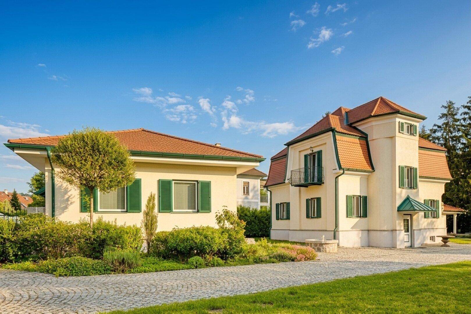 Seitenansicht des Hauses mit gepflasterter Auffahrt und angrenzendem Nebengebäude im Sonnenlicht.